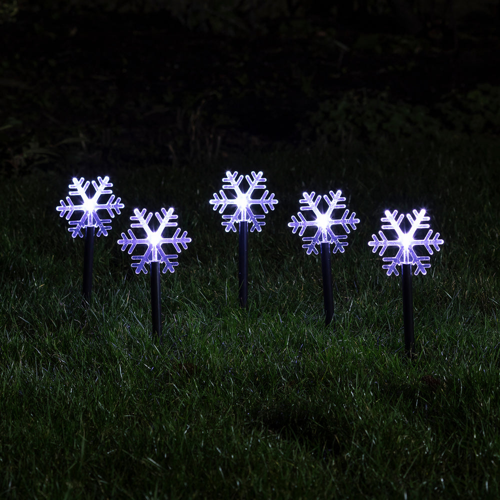 Fünf leuchtende Schneeflocken Stableuchten mit weißen LEDs im dunklen Garten auf grünem Gras