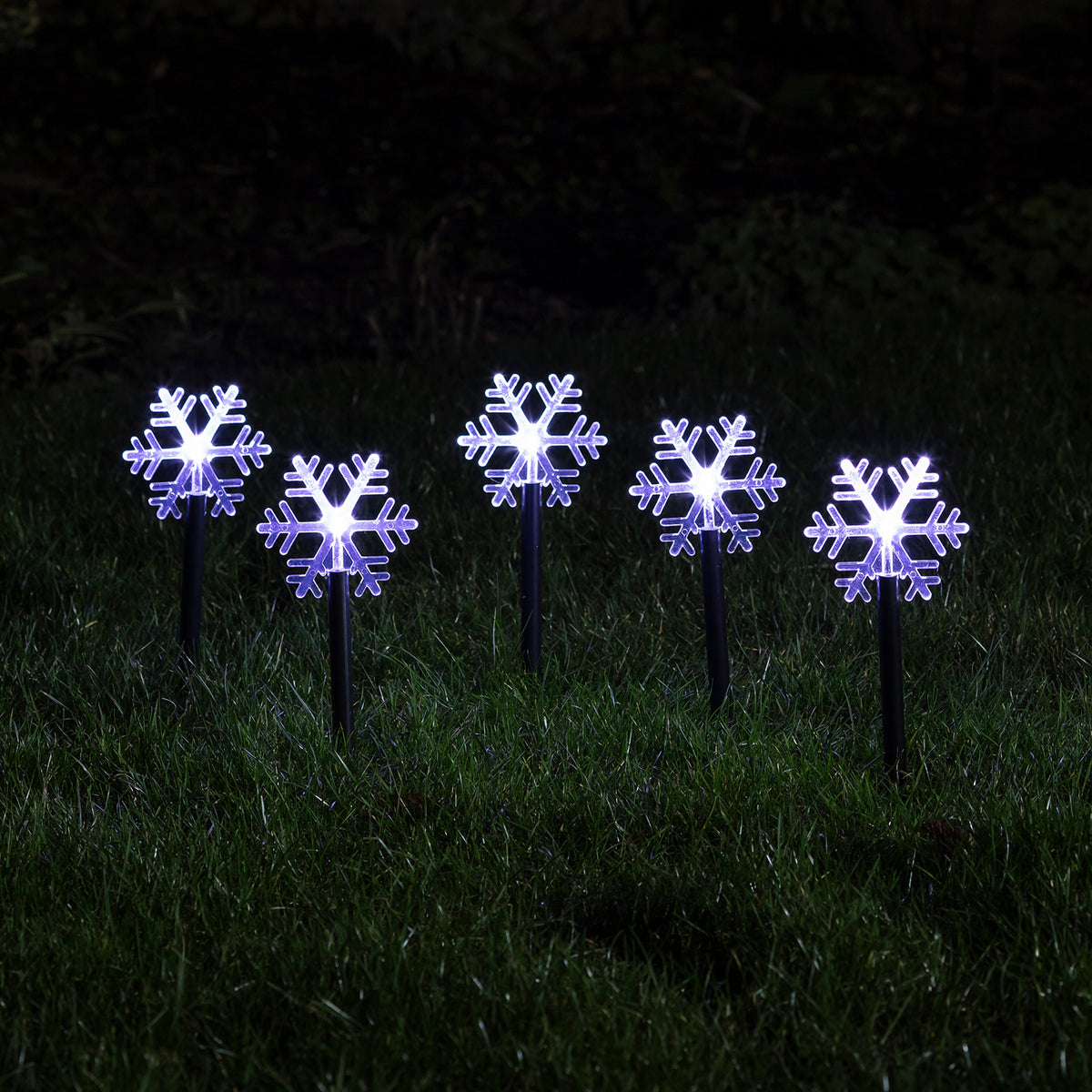 Fünf leuchtende Schneeflocken Stableuchten mit weißen LEDs im dunklen Garten auf grünem Gras