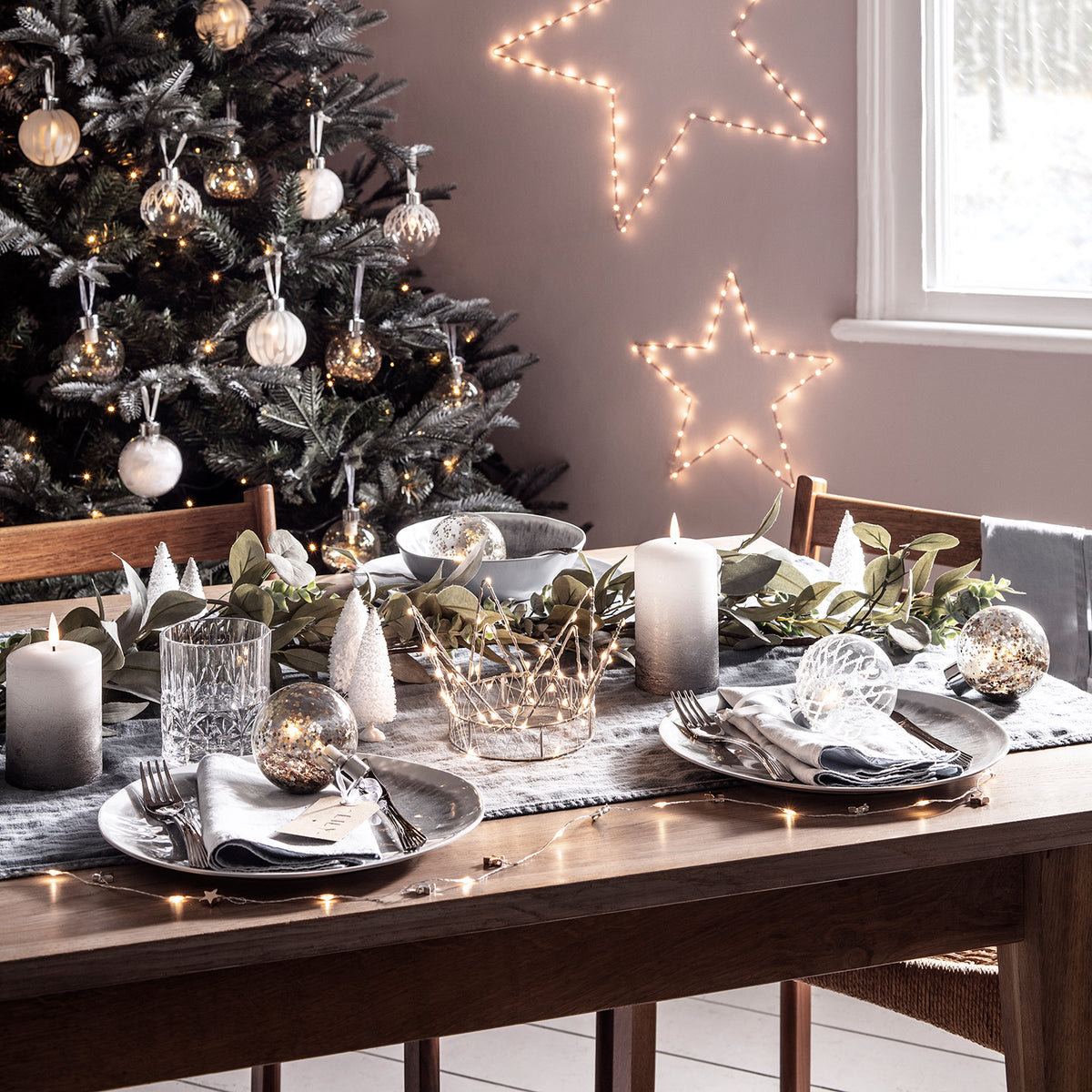 Leuchtender LED-Stern in Roségold an Wand neben festlich gedecktem Esstisch und Weihnachtsbaum