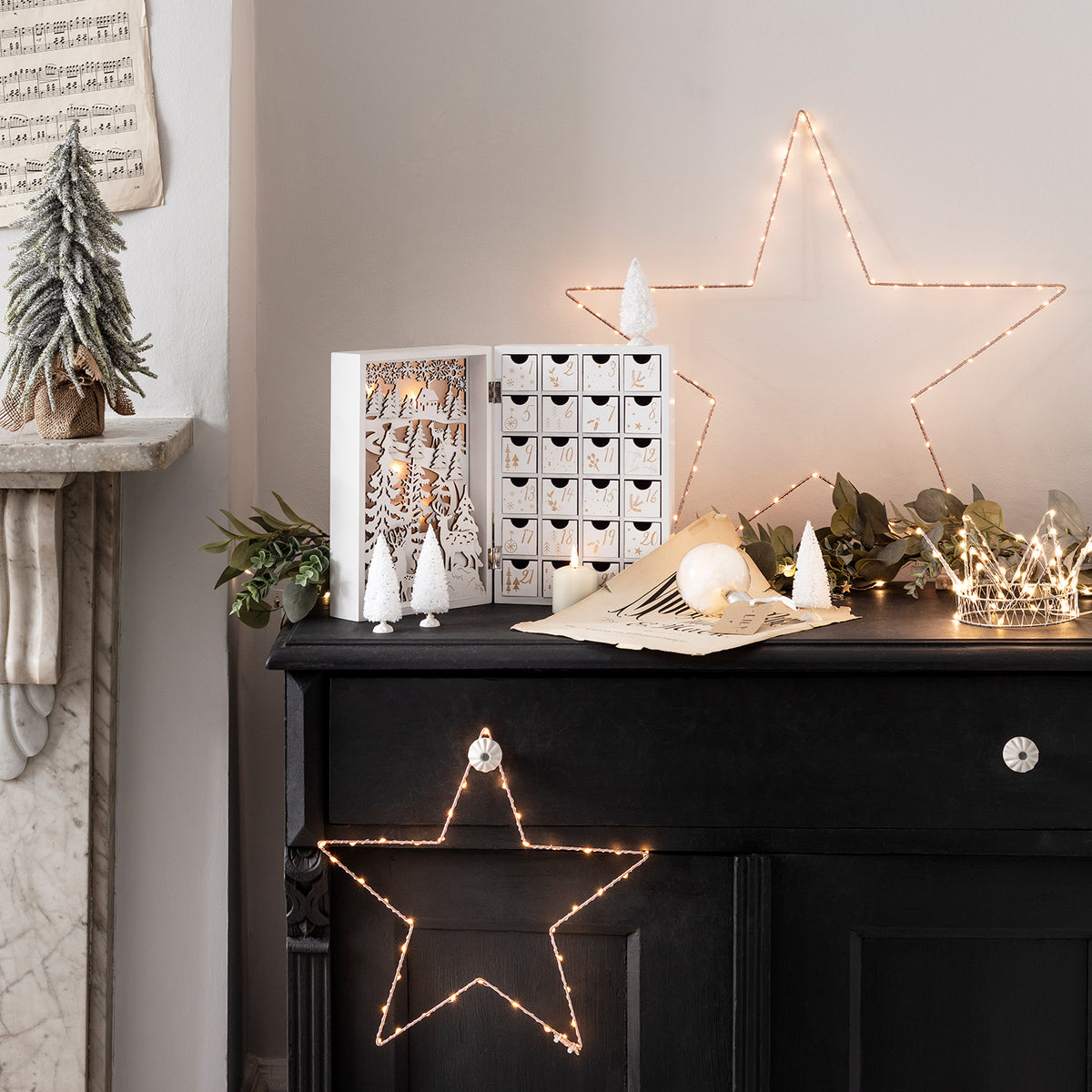 Großer LED-Stern in Roségold neben Adventskalender und Weihnachtsdeko auf schwarzem Sideboard