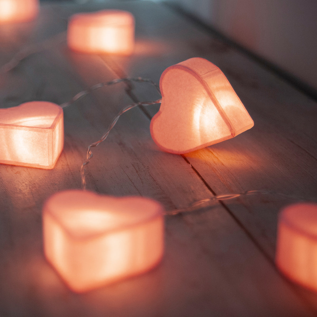 Warmweiß leuchtende Papierherzen auf einer Lichterkette auf Holzoberfläche