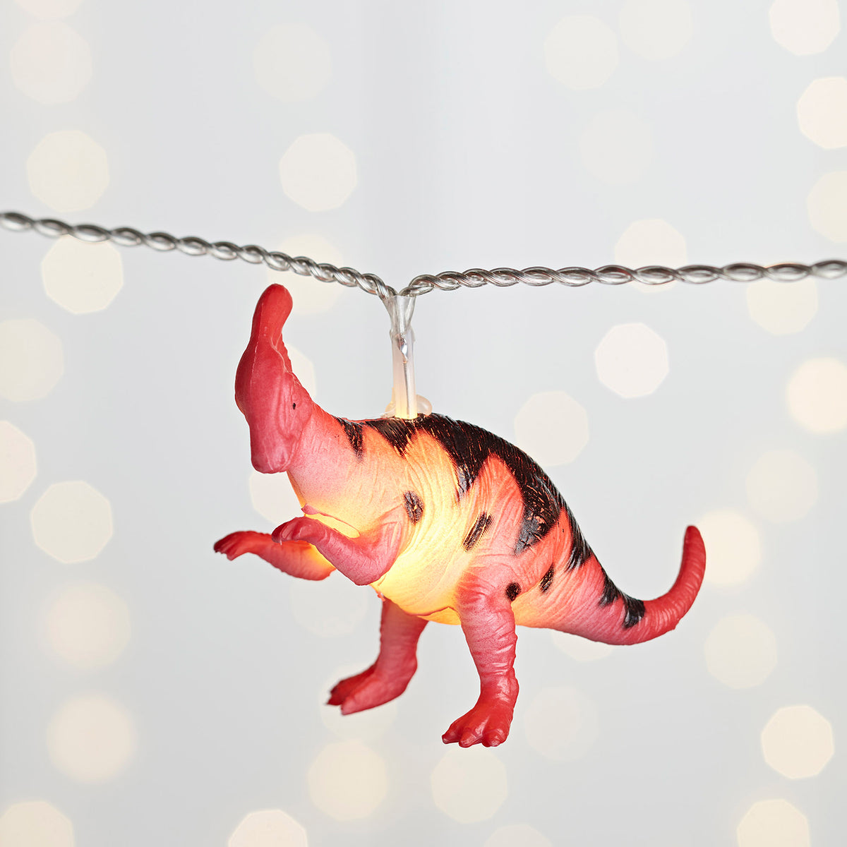 Leuchtender roter Dinosaurier Anhänger an Lichterkette vor hellem Hintergrund