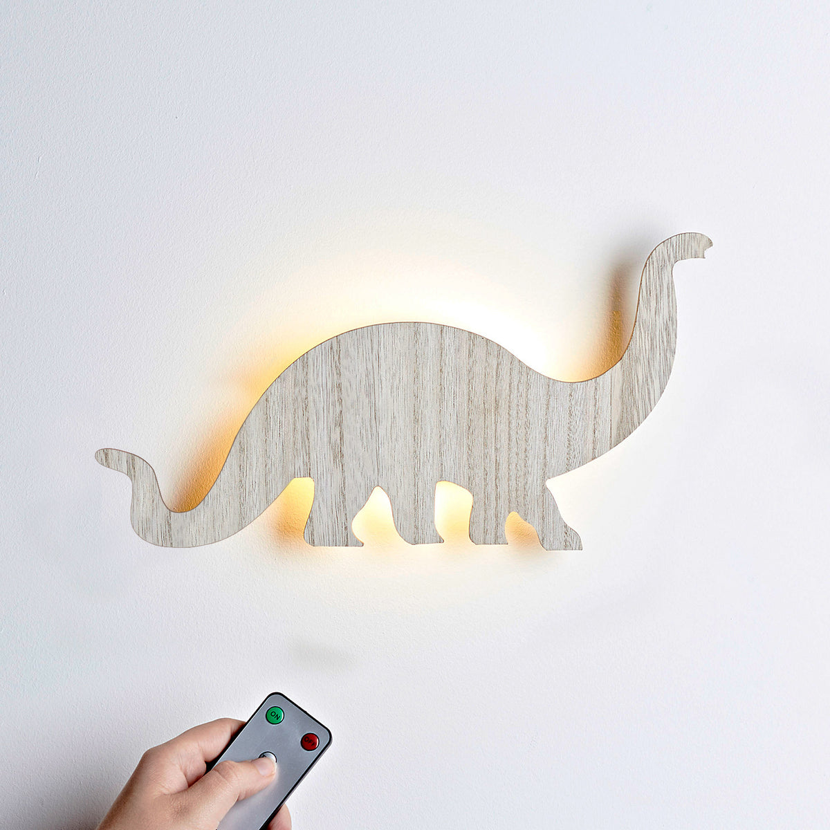 Hand hält Fernbedienung vor beleuchtete Holz Wandlampe in Dinosaurierform