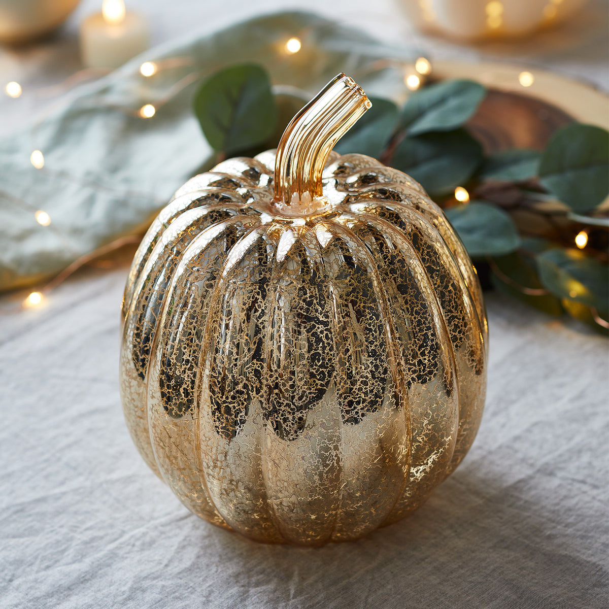 Leuchtender antikgoldener Glas-Kürbis auf Holzscheibe mit Kerzen und herbstlicher Dekoration