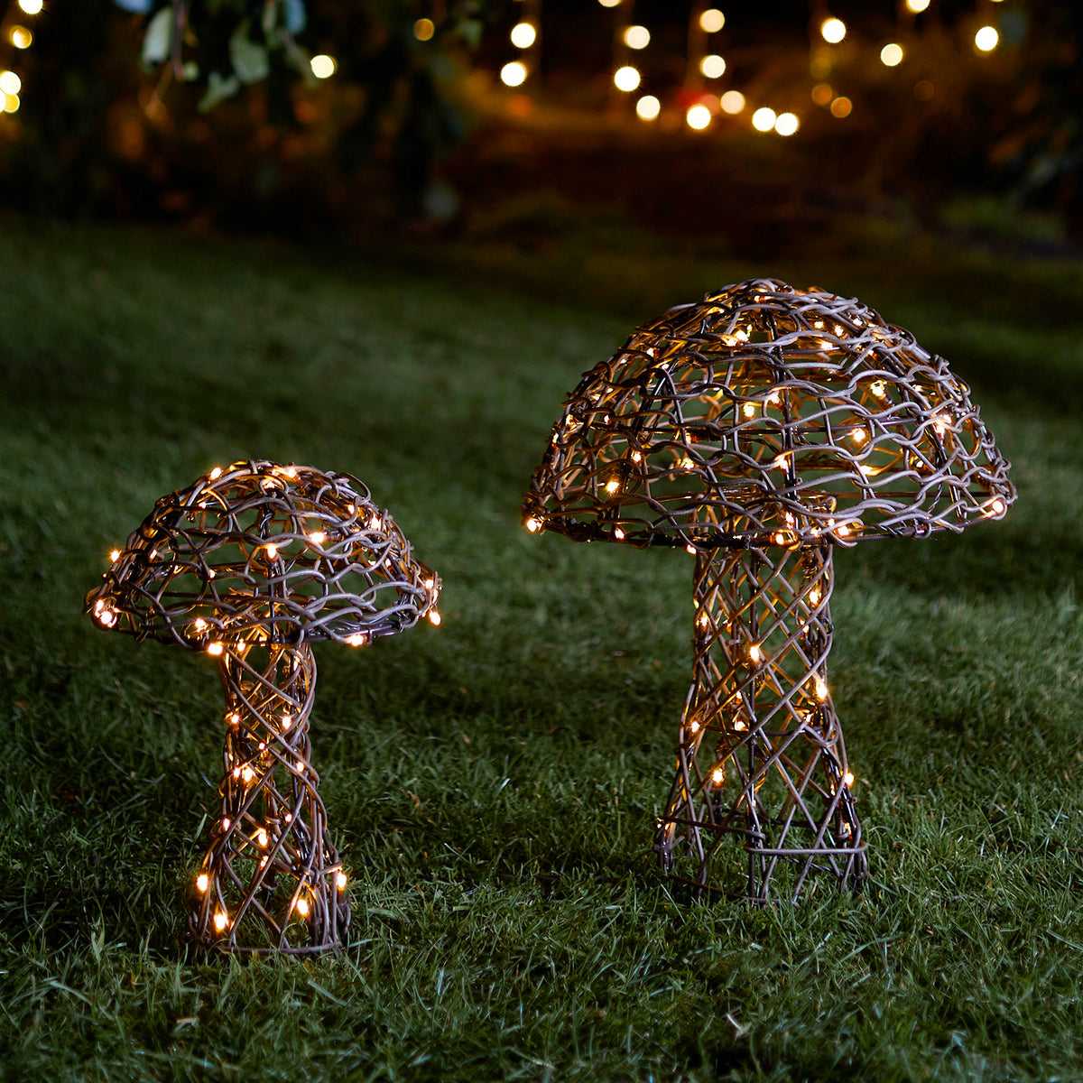 Zwei beleuchtete Rattan-Pilze mit warmweißen LEDs auf grünem Rasen bei Dämmerung