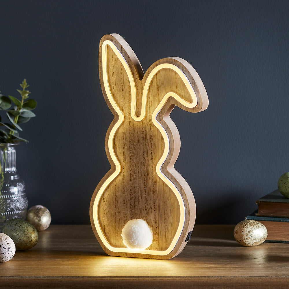 Seitliche Ansicht der Holz-Hasenlampe mit warmweißem Neonlicht und weißem Bommel auf Holzfläche