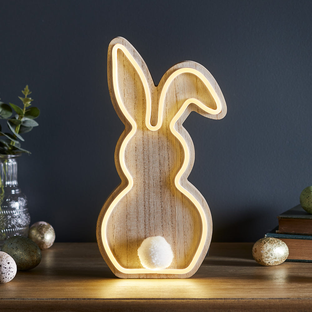 Holzlampe in Hasenform mit warmweiß leuchtendem Neonschlauch und weißem Bommel als Schwanz