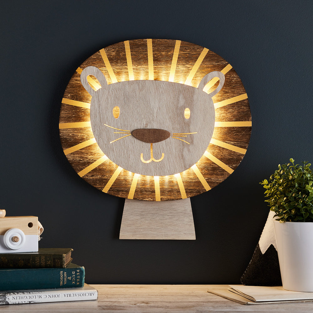 Leuchtende Löwen Wandlampe mit warmweißen LEDs an dunkler Wand, dekoriert mit Büchern und Pflanze