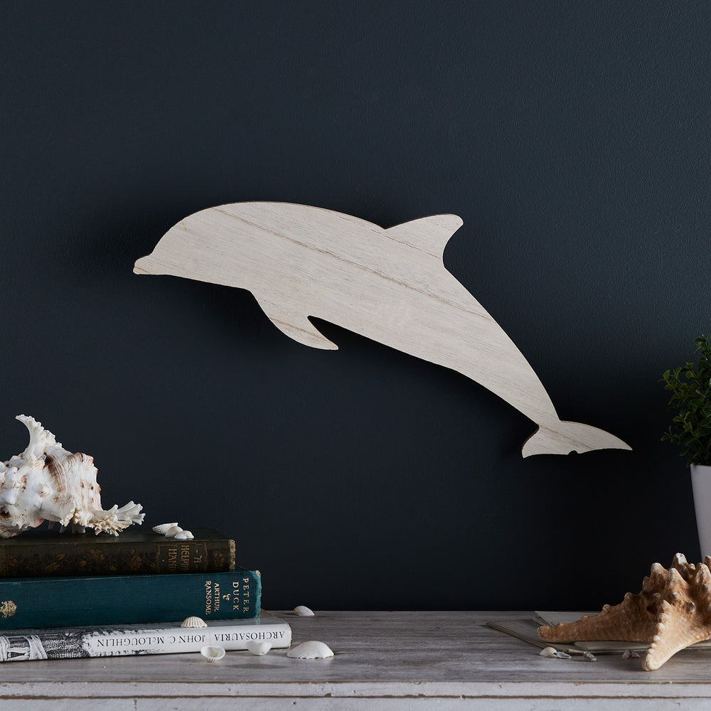 Holzlampe in Delfinform ohne Licht an dunkler Wand mit Muscheldeko