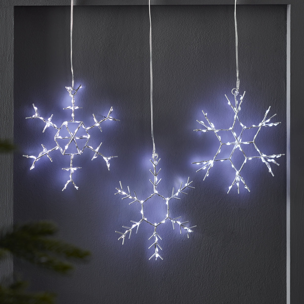 Drei leuchtende LED-Schneeflocken aus Metall vor dunkler Wand hängend