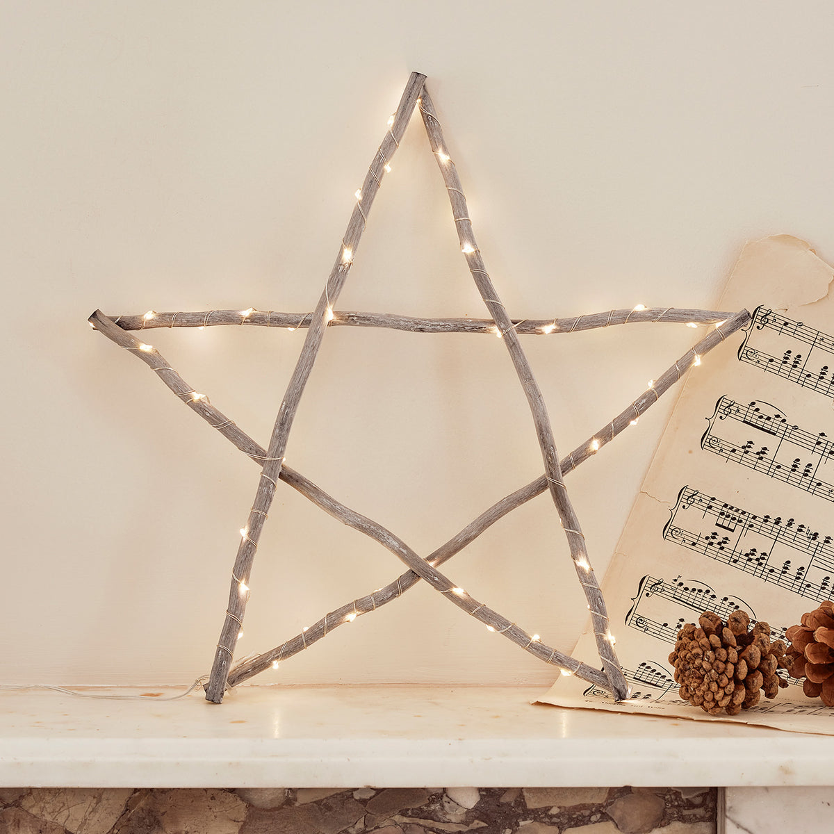 Holzstern mit LED-Lichterkette vor Wand mit Notenblatt und Tannenzapfen
