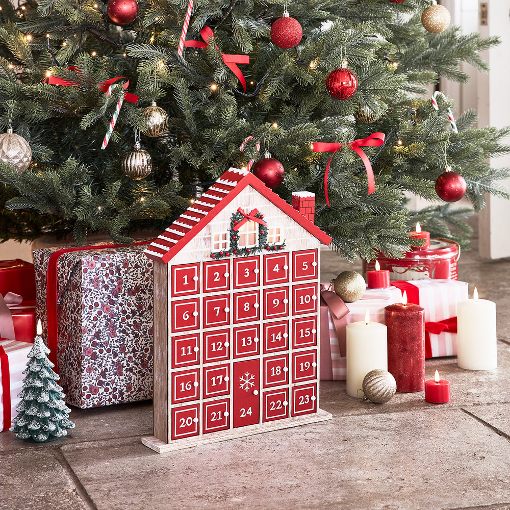 Winterlicher Adventskalender vor geschmücktem Weihnachtsbaum mit Kerzen und Geschenken