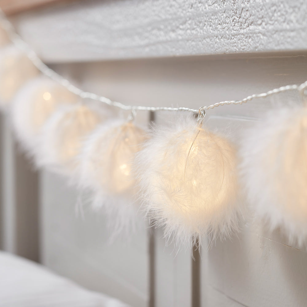 Flauschige weiße Bälle mit warmweißem Licht an einer Lichterkette am Kopfteil eines Bettes