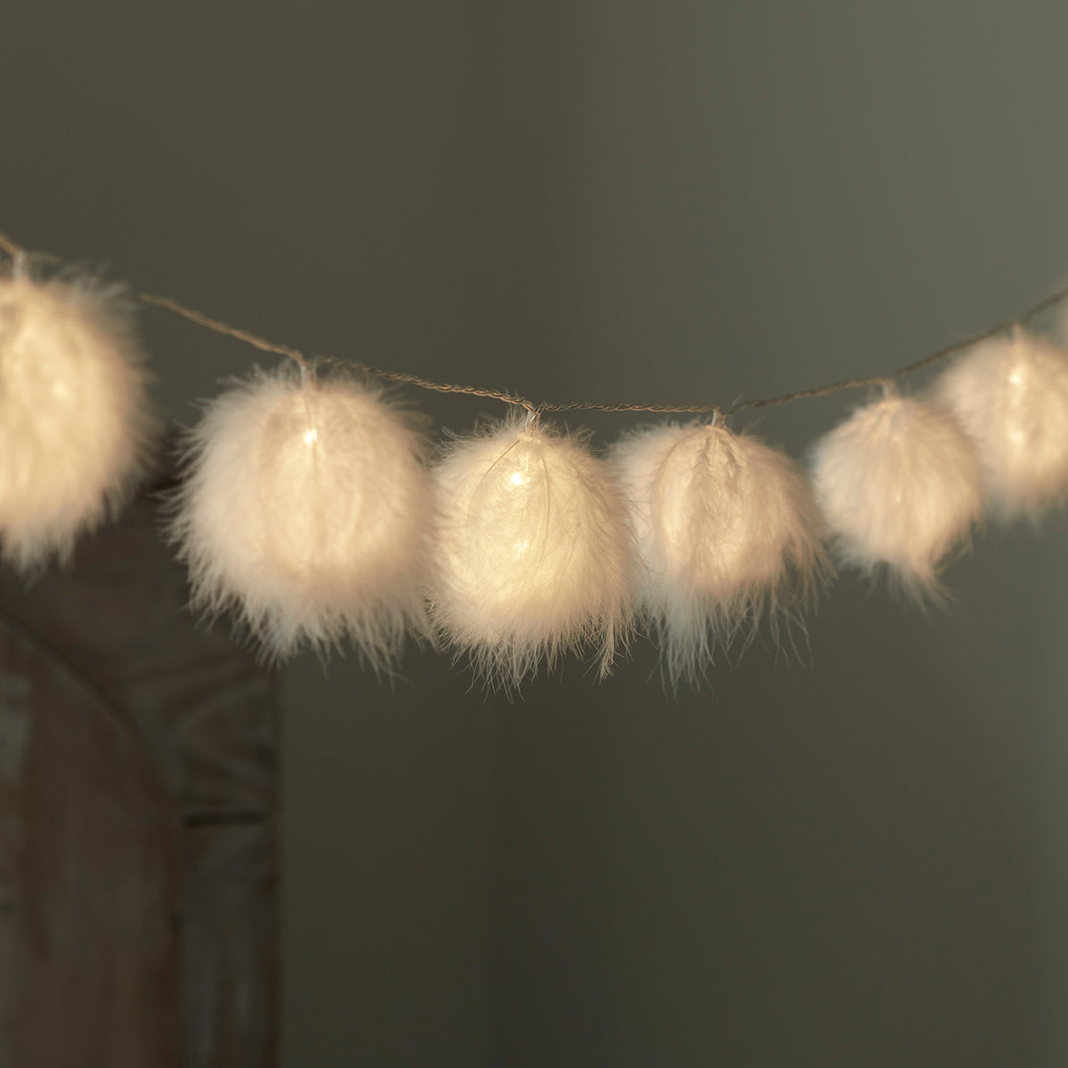 Flauschige weiße Bälle mit warmweißem Licht an einer Lichterkette vor dunklem Hintergrund