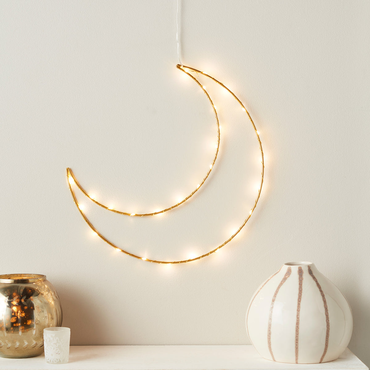 Goldener Metallrahmen in Mondform mit warmweißen LEDs an weißer Wand über Kommode