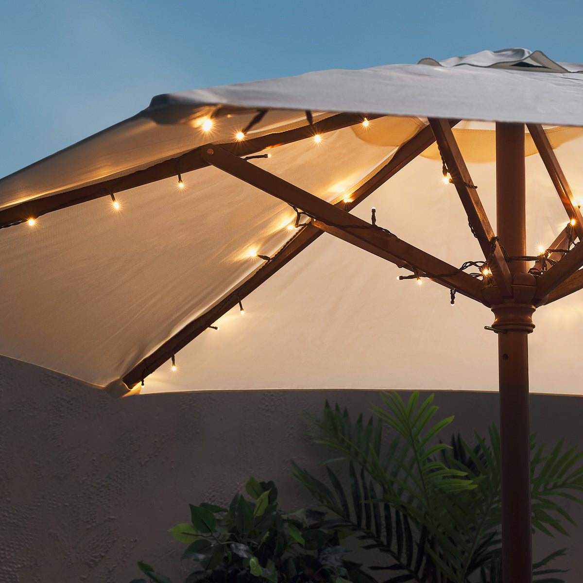 Warmweiße LED-Lichterkette umrahmt die Holzbalken eines geöffneten Sonnenschirms bei Abenddämmerung