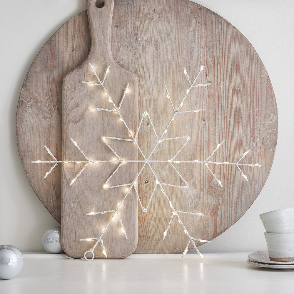 Leuchtende LED-Schneeflocke auf Holzbrett vor rundem Holzbrett stehend