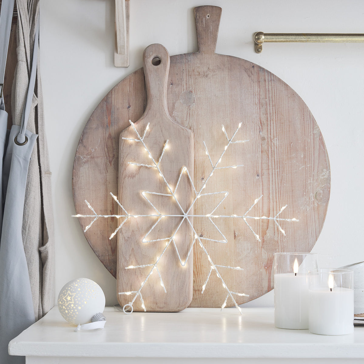 LED-Schneeflocke auf Holzbrett vor rundem Holzbrett mit Kerzen und Weihnachtskugel