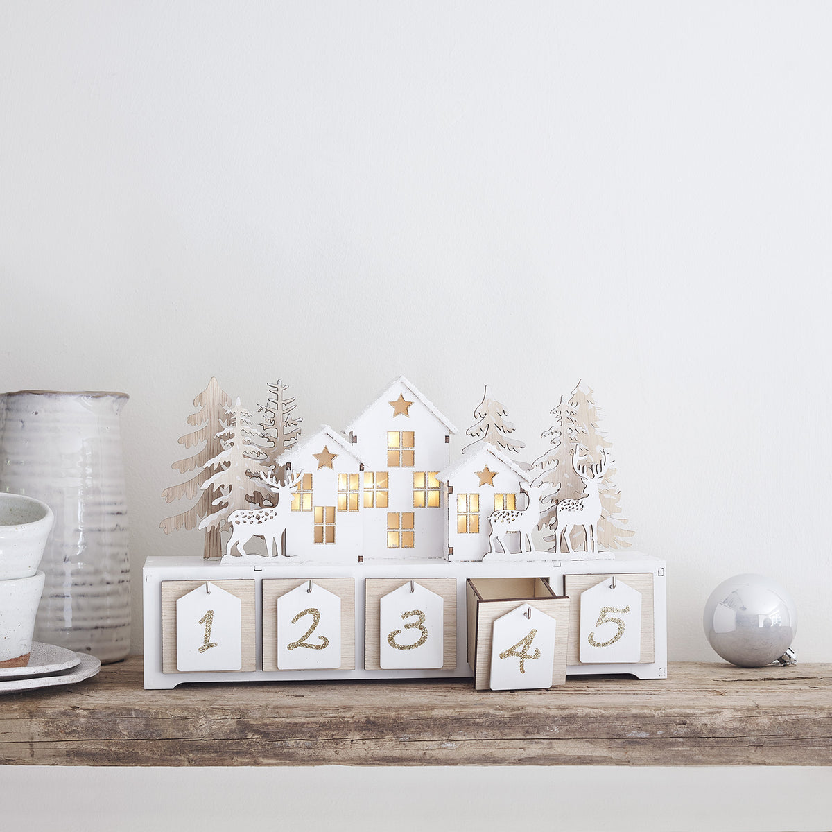 Holzadventskalender mit beleuchteten Häusern, Rentieren und Tannenbäumen auf Holzablage