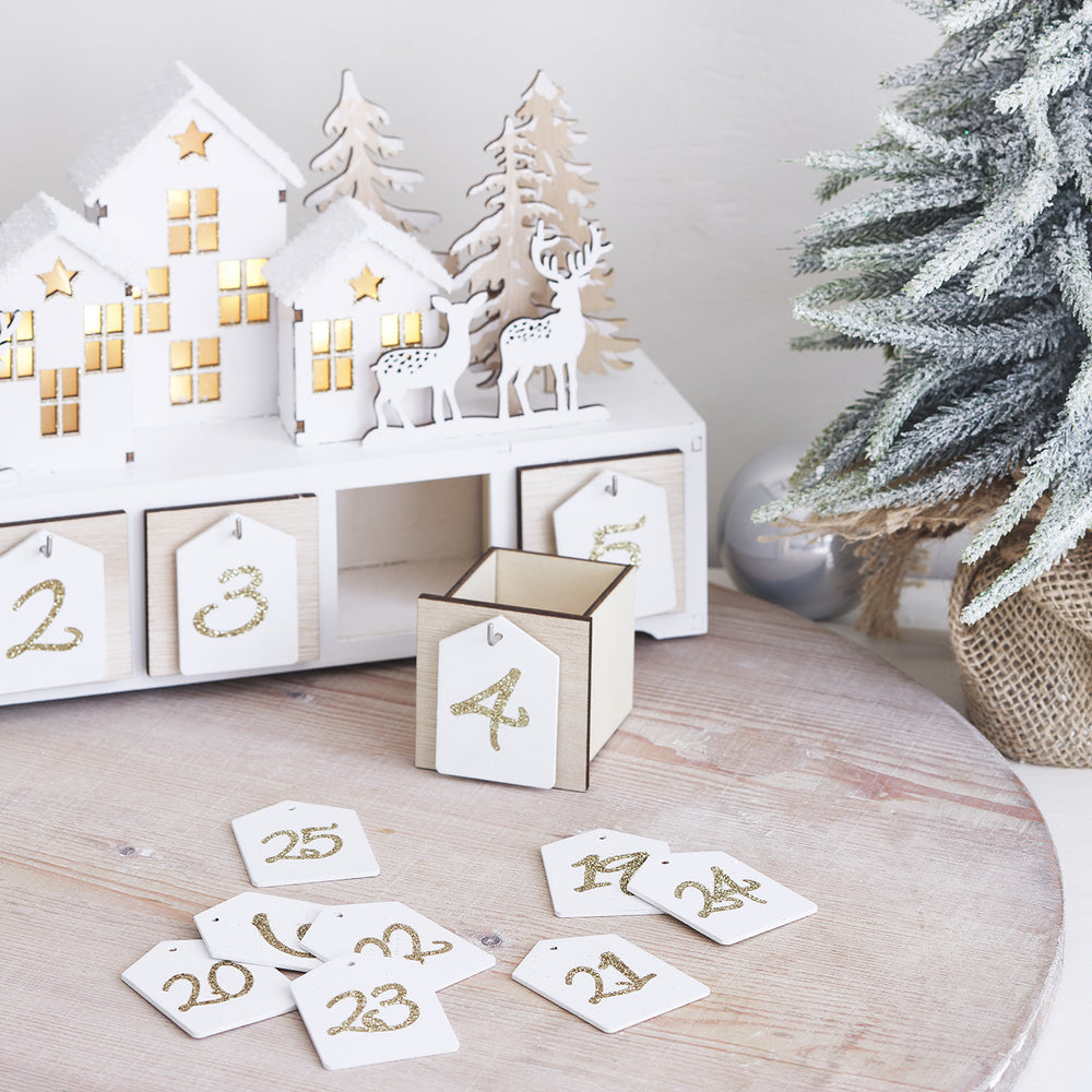 Adventskalender mit offener Schublade und goldglitzernden Zahlen vor künstlichem Tannenbaum