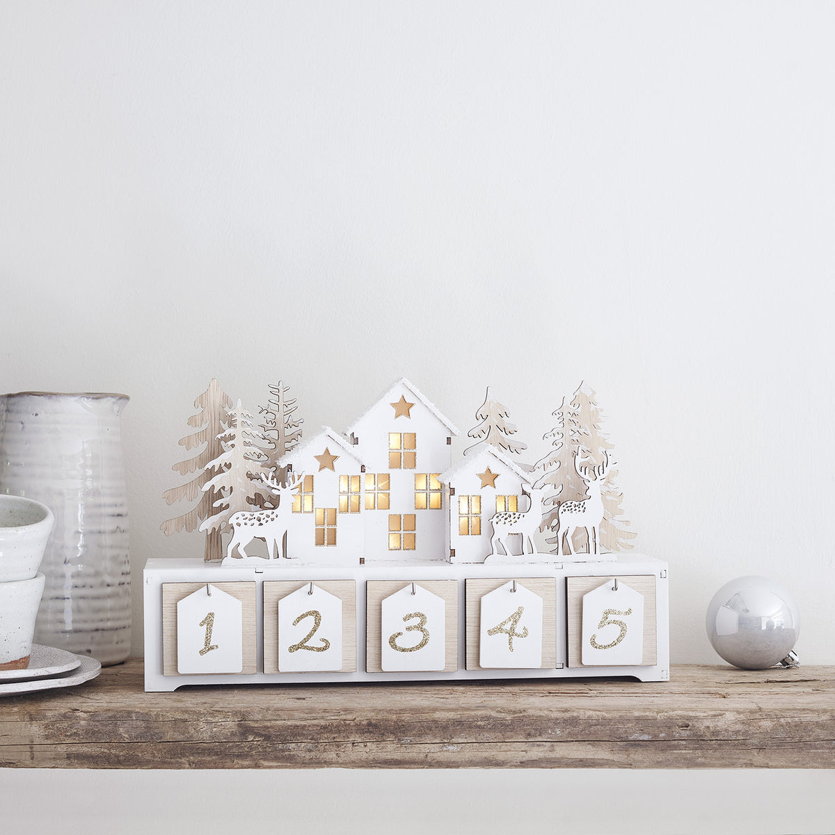 Holzadventskalender mit warmweißen LEDs in Fenstern und filigranen Rentieren auf Holzregal