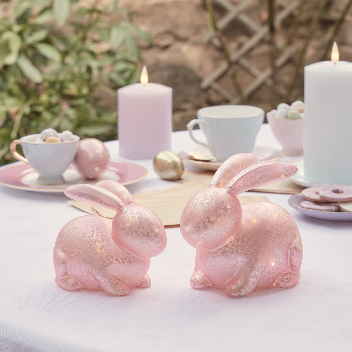 Zwei pastellrosa Glashasen mit LED-Beleuchtung auf einem gedeckten Ostertisch