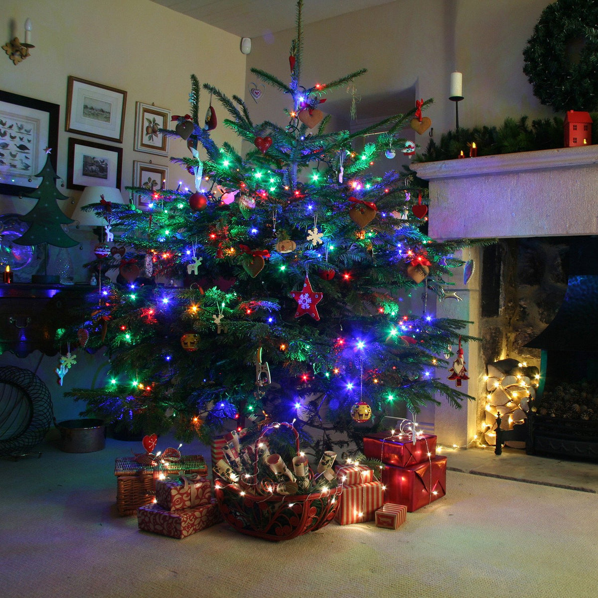 Weihnachtsbaum im Wohnzimmer mit bunten Lichtern, Dekorationen und Geschenken neben Kamin
