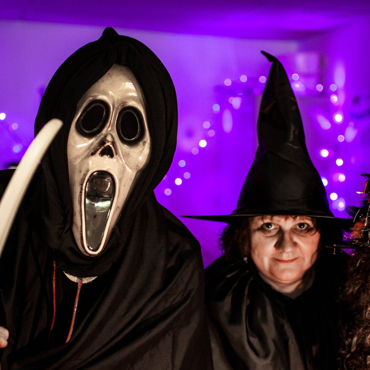 Personen in Halloween-Kostümen vor lila beleuchteter Wand mit LED-Lichterkette