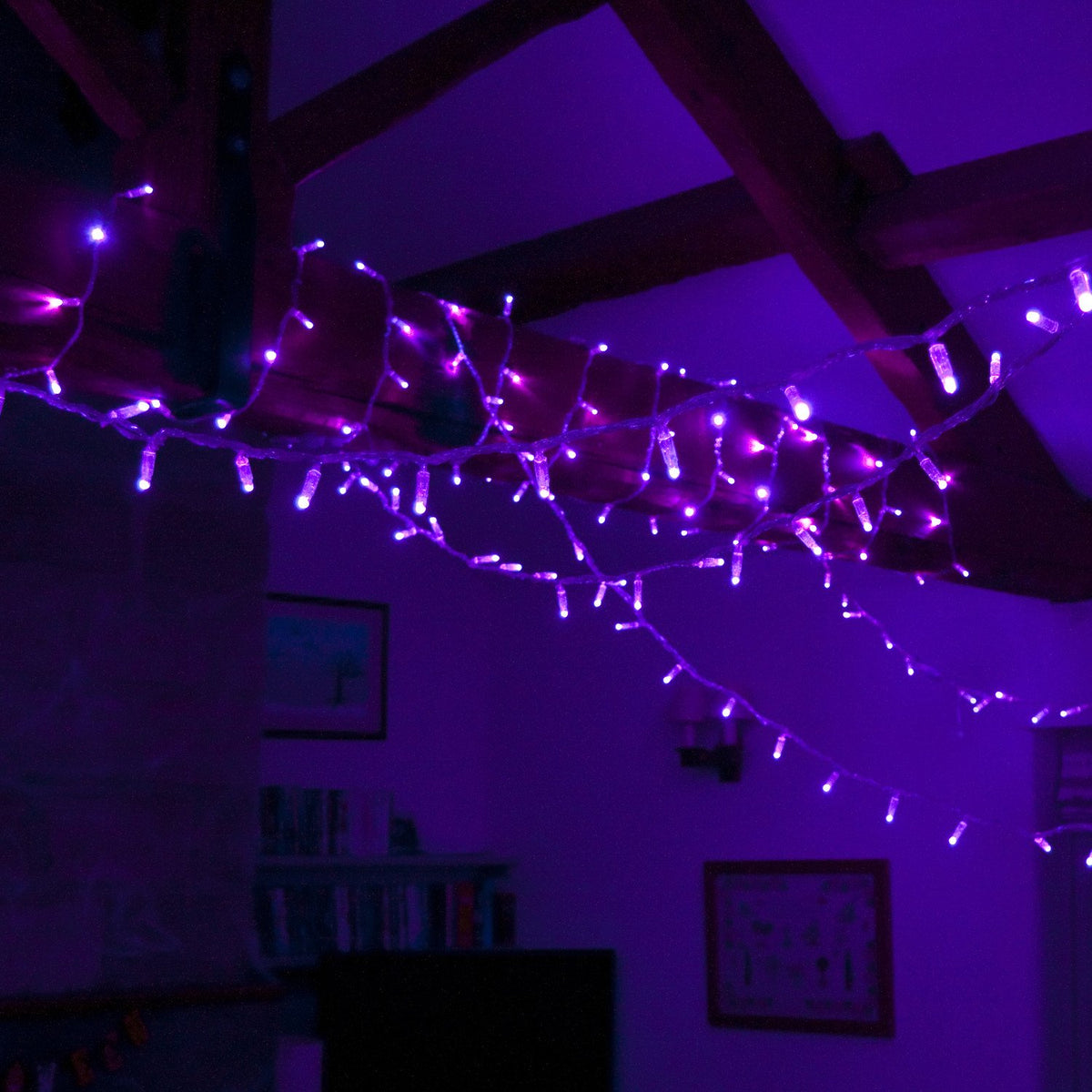 Lila LED-Lichterkette hängt von Holzbalken in einem Raum mit Vorhängen