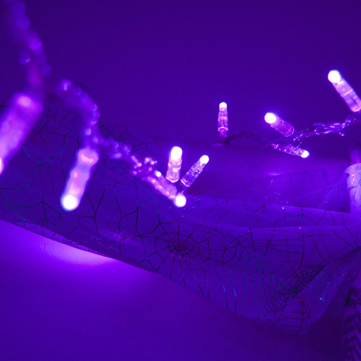 Lila LED-Lichterkette mit Spinnennetz-Dekoration an Holzbalken im Raum