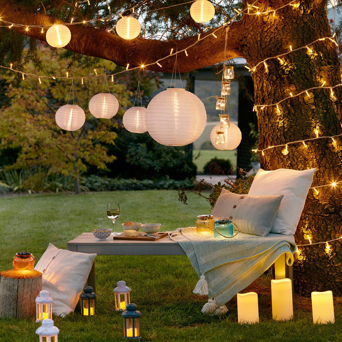 Gemütliche Gartenlounge mit Lichterketten, Papierlaternen und Kissen