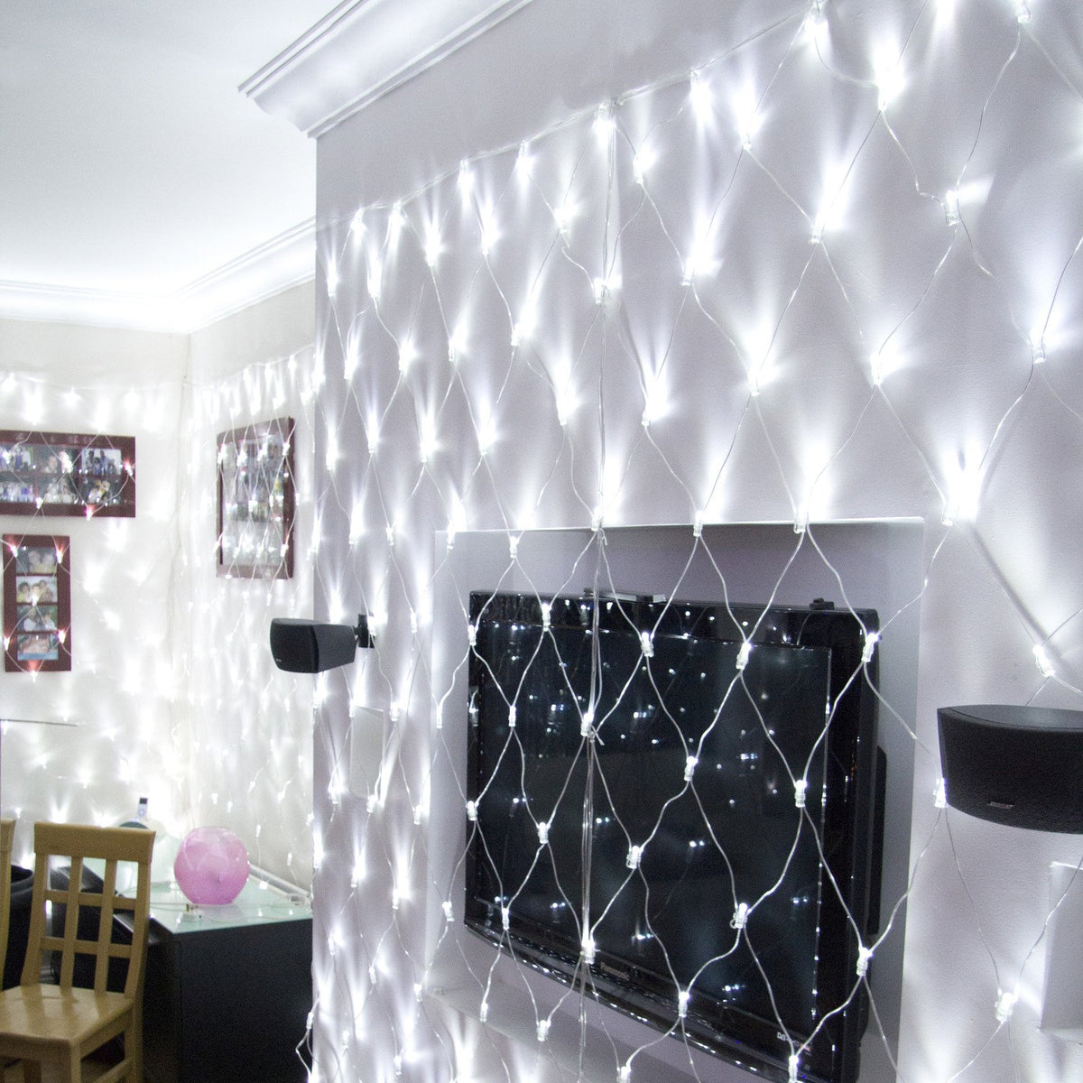 Weißes LED Lichternetz hängt beleuchtet an Wand über Fernseher und Lautsprecher