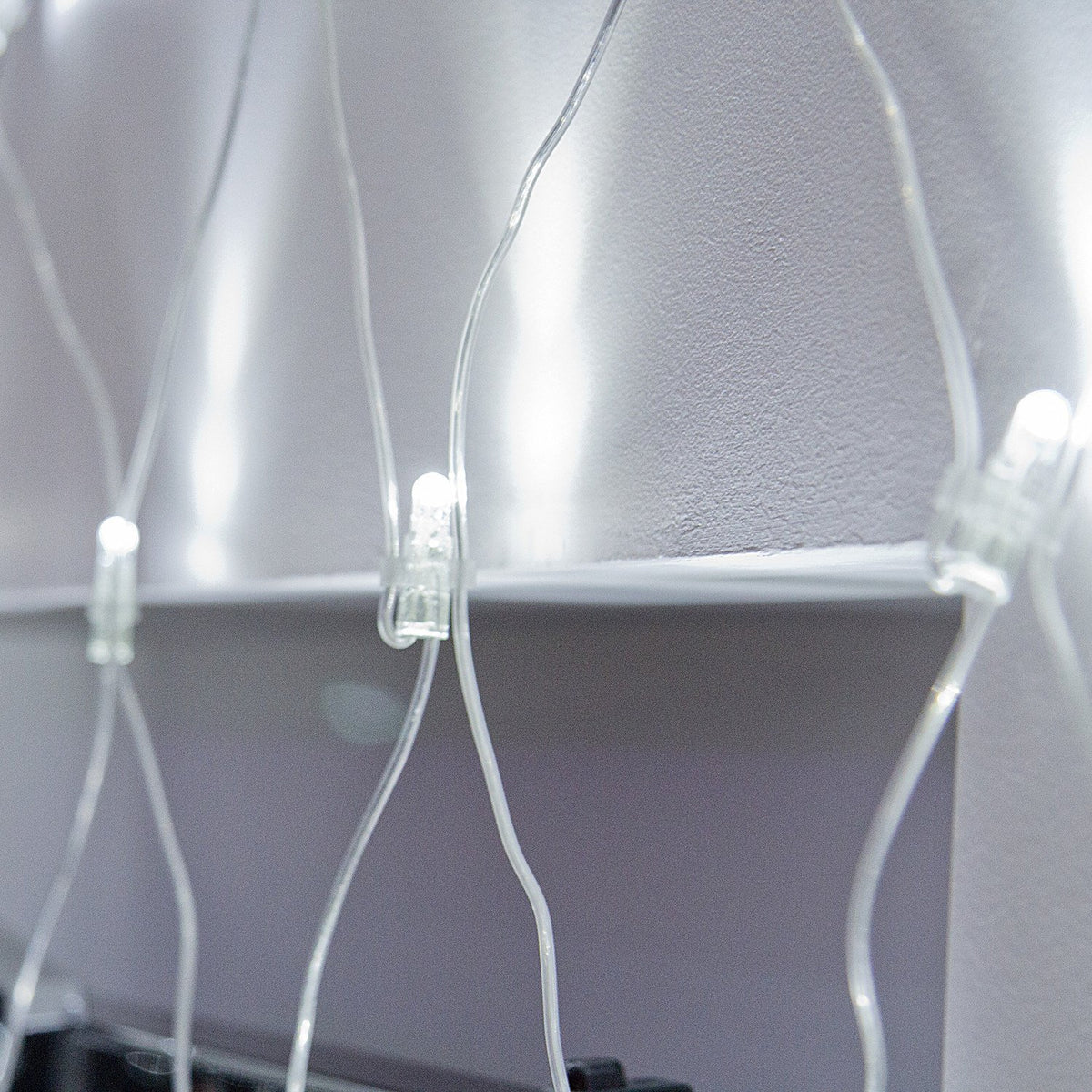 Detailaufnahme eines Steckverbinders am transparenten Kabel des weißen LED-Lichternetzes