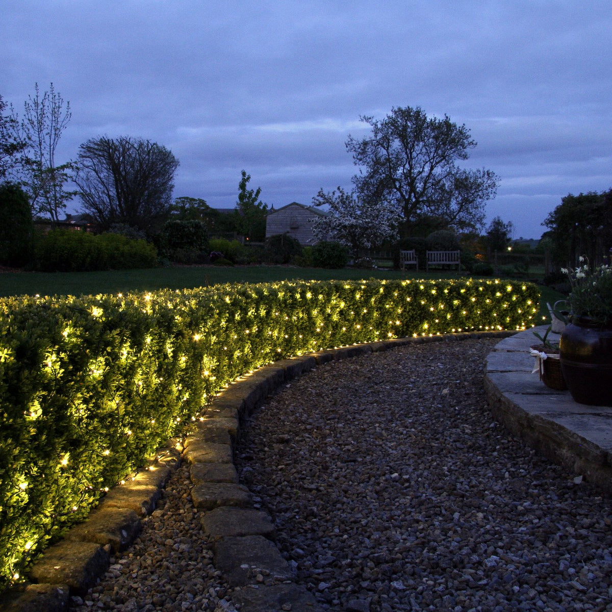 LED-Lichternetz mit warmweißen Lichtern dekoriert Hecke entlang Gartenweg
