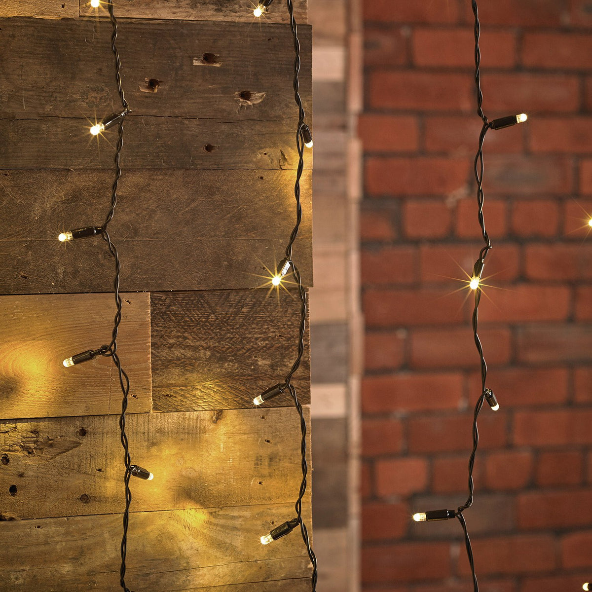 Nahaufnahme von warmweißen LED-Lichtervorhängen mit schwarzem Kabel vor Holz- und Backsteinwand