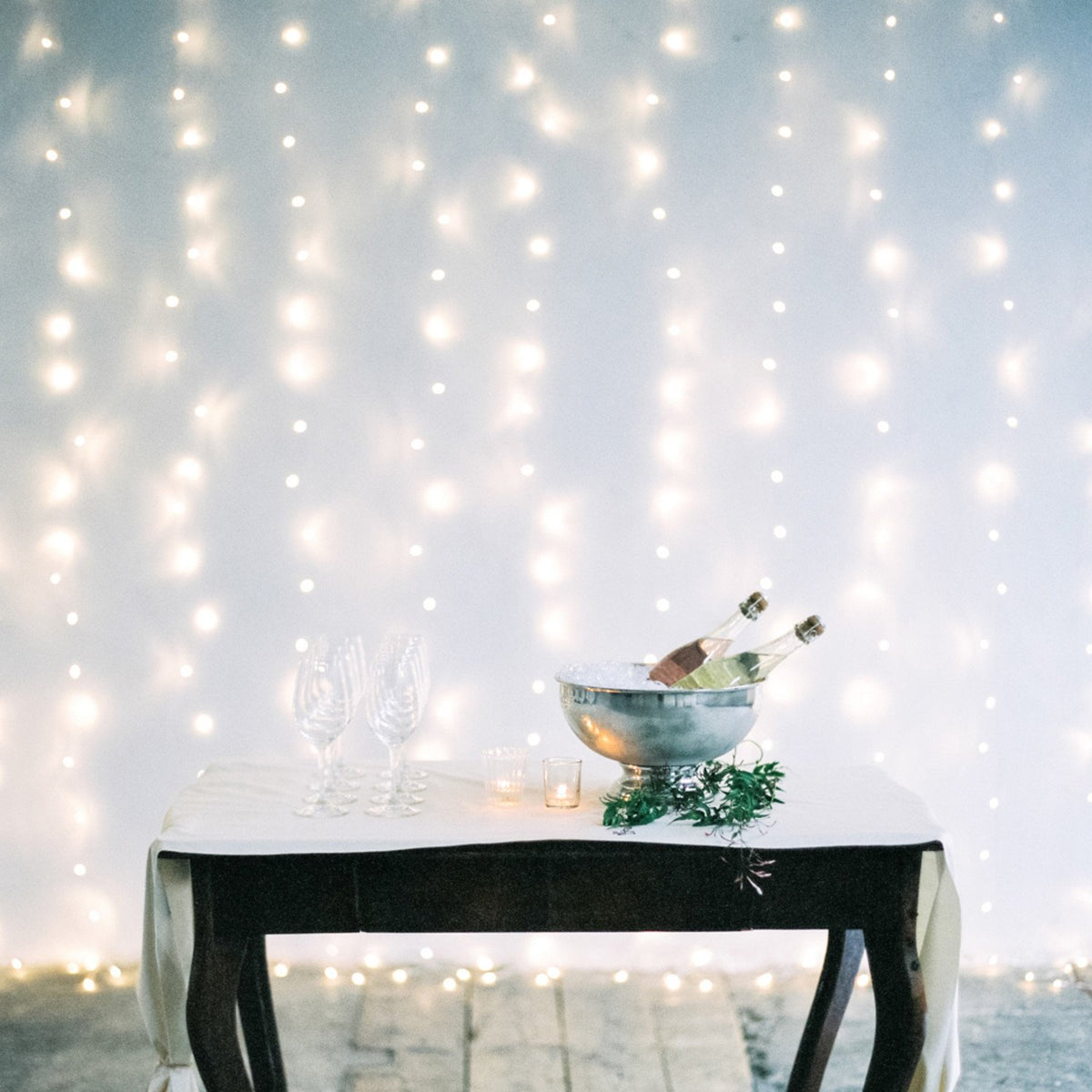 Warmweißer LED-Lichtervorhang als Hintergrunddekoration hinter einem Tisch mit Champagner und Gläsern