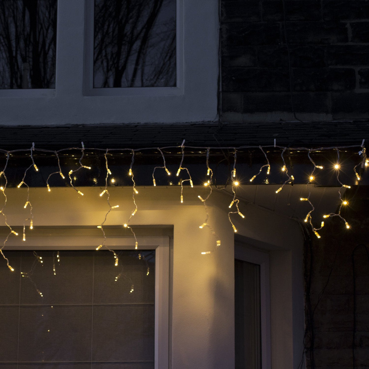 Warmweiße Eiszapfen Lichterkette an Dachrinne eines Hauses bei Nacht
