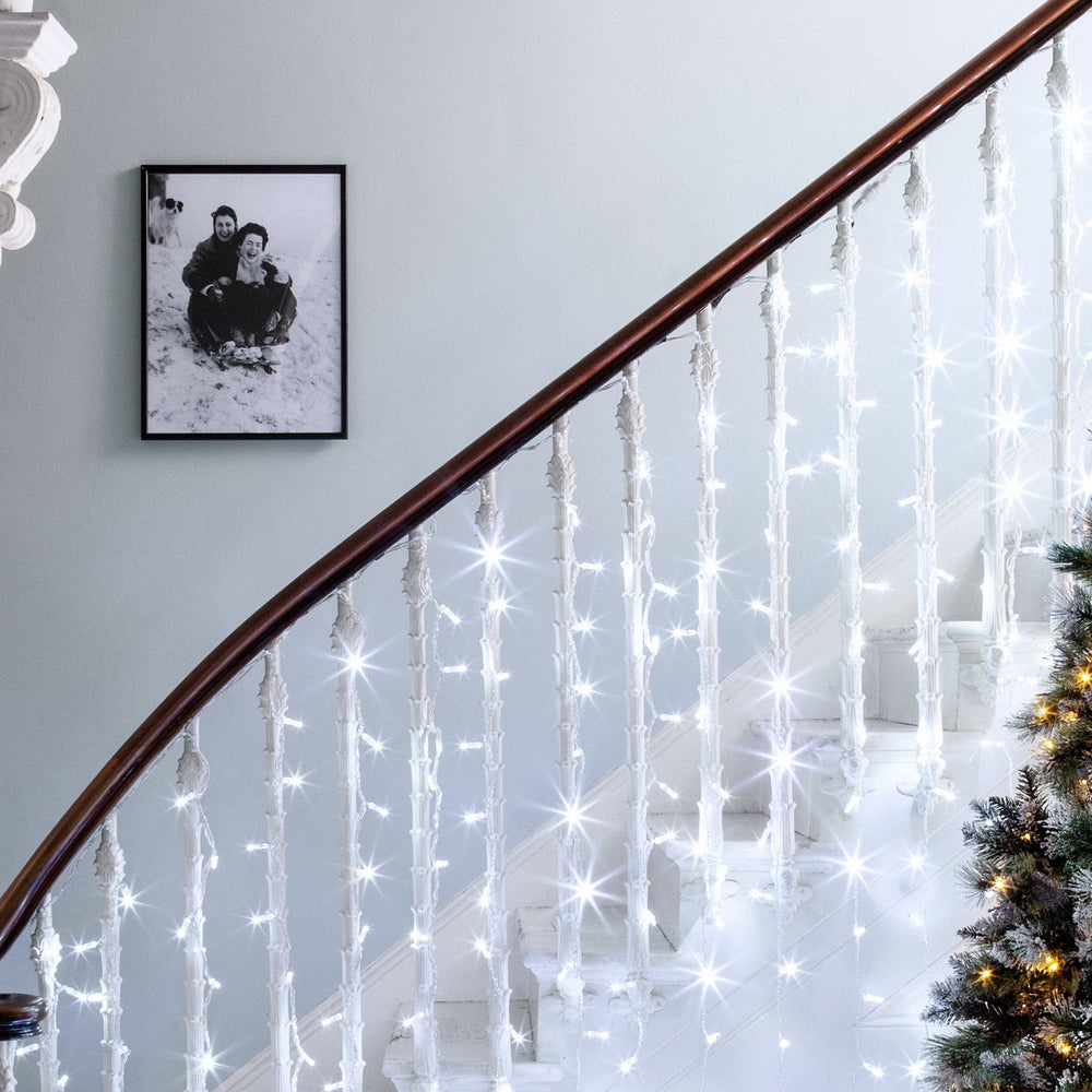Weißer LED-Lichtervorhang hängt an einem weißen Treppengeländer mit Holzhandlauf