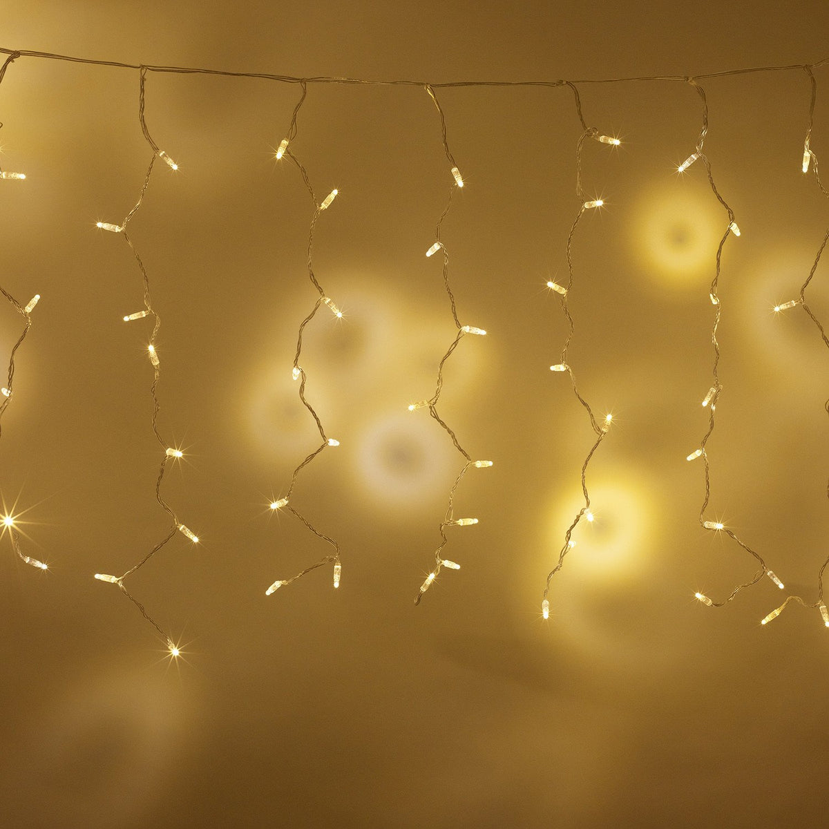 Warmweiße LED-Lichtervorhänge vor unscharfem gelbem Hintergrund mit Lichtreflexionen