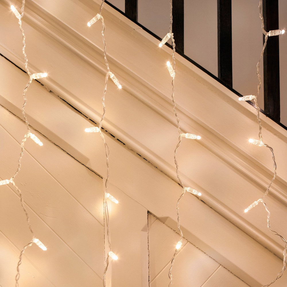 Warmweiße LED-Lichtervorhänge mit transparentem Kabel an einer weißen Wand und Treppe