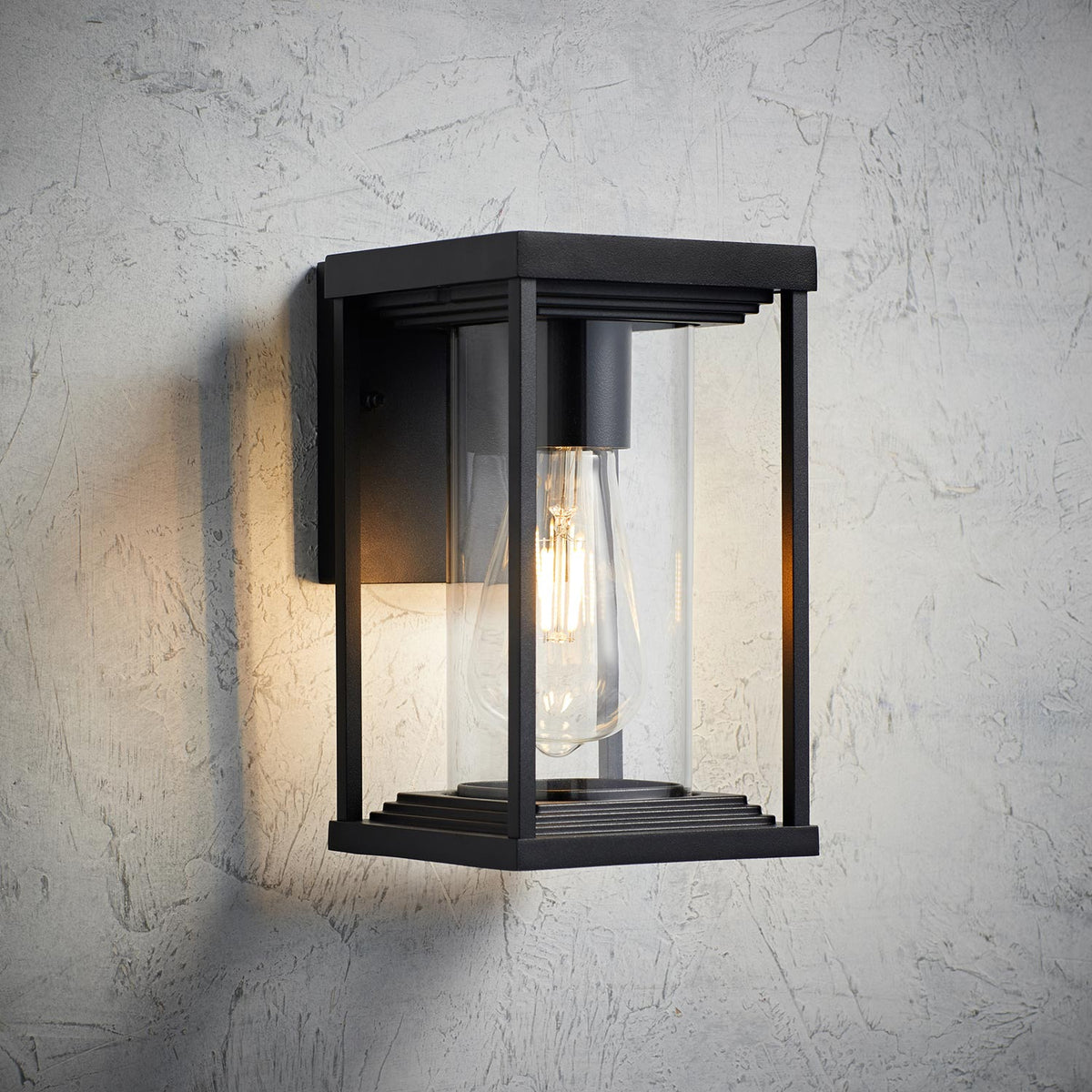 Schwarze laternenförmige Außenwandleuchte mit Glas und sichtbarer E27 Glühbirne an strukturierter Wand