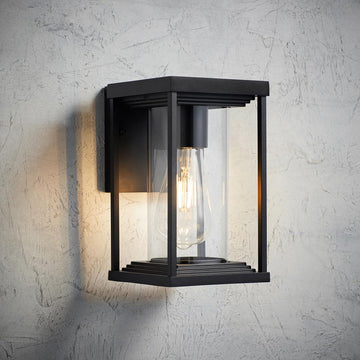 Schwarze laternenförmige Außenwandleuchte mit Glas und sichtbarer E27 Glühbirne an strukturierter Wand