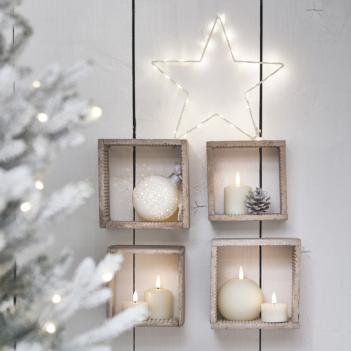 LED Stern in Holzrahmen an weißer Wand mit Kerzen und Weihnachtskugel