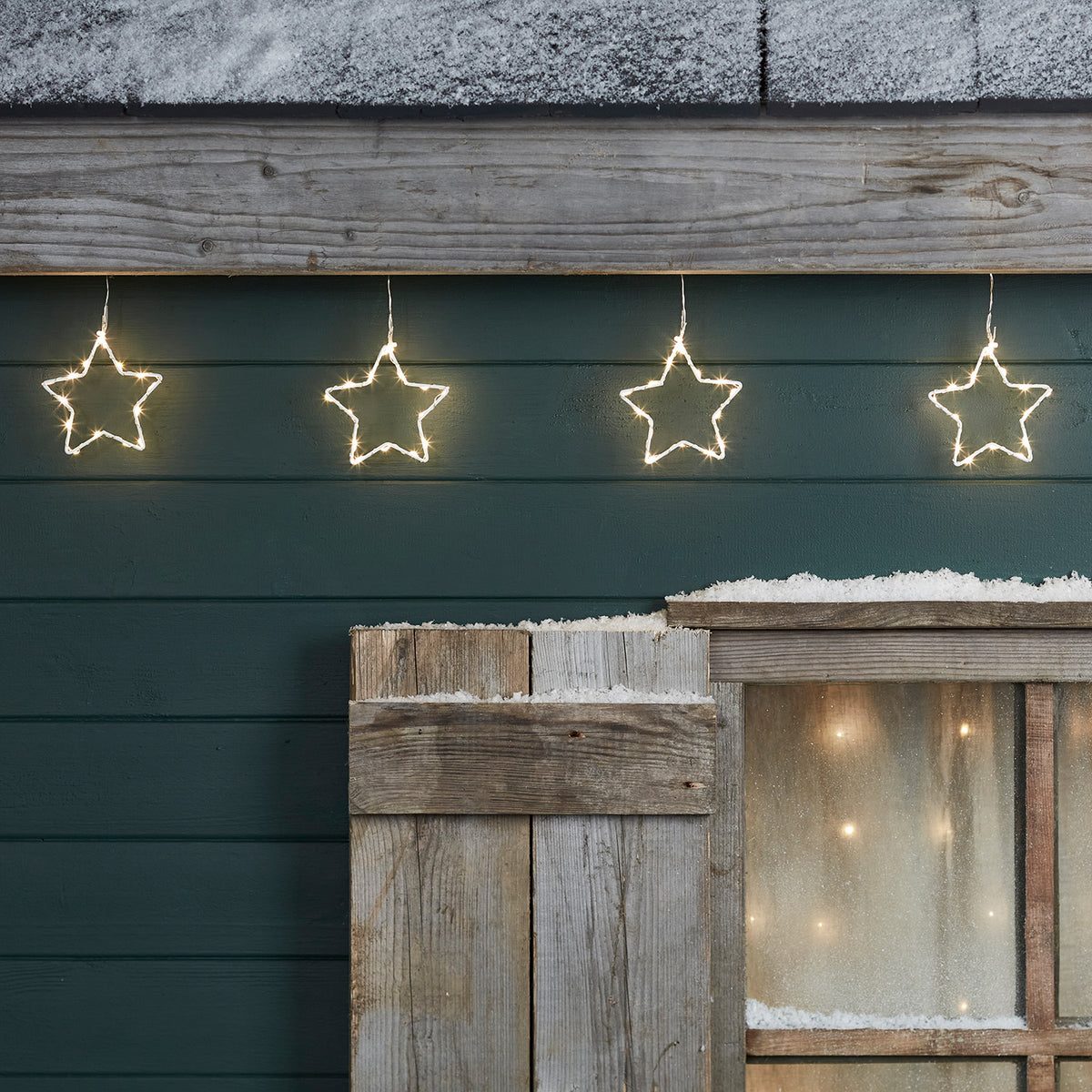 Vier LED-Sterne an einer Lichterkette vor einer grünen Holzfassade mit Fensterläden
