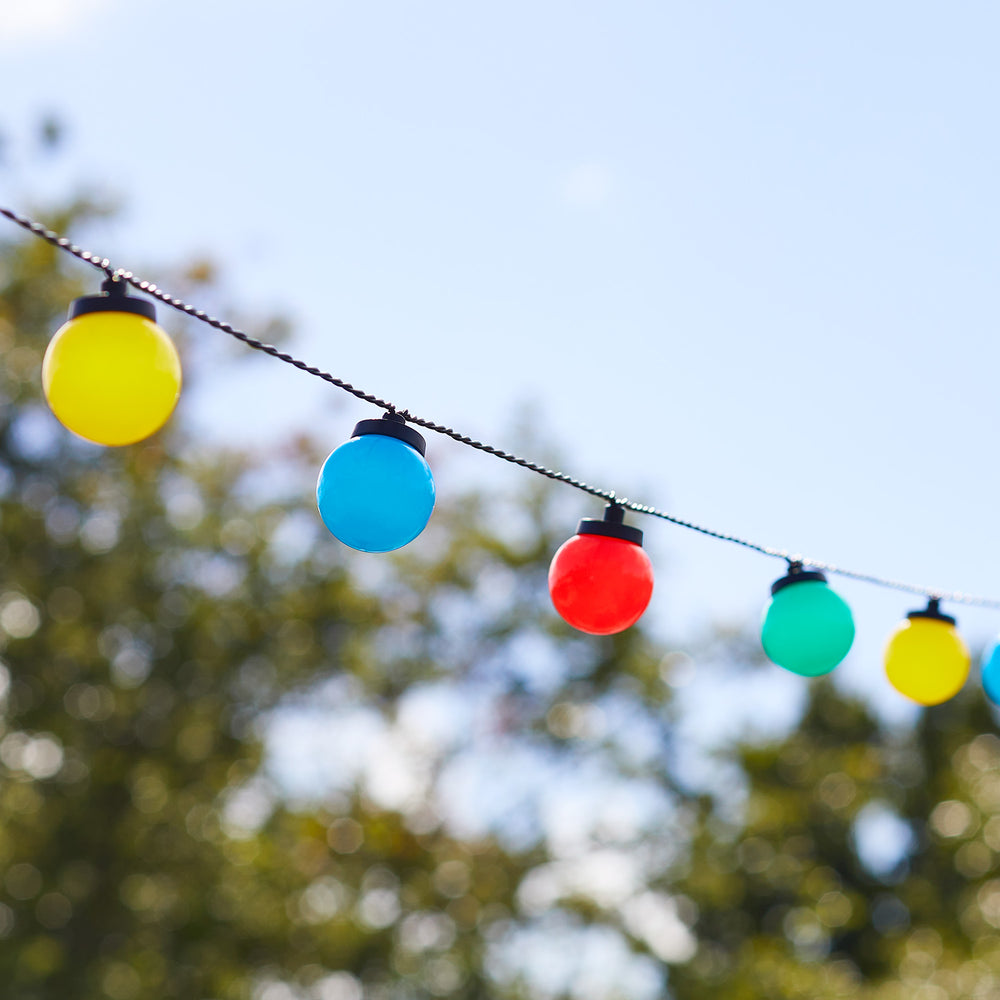 Bunte Kugel-Lichterkette mit gelben, blauen, roten und grünen Lampen vor blauem Himmel