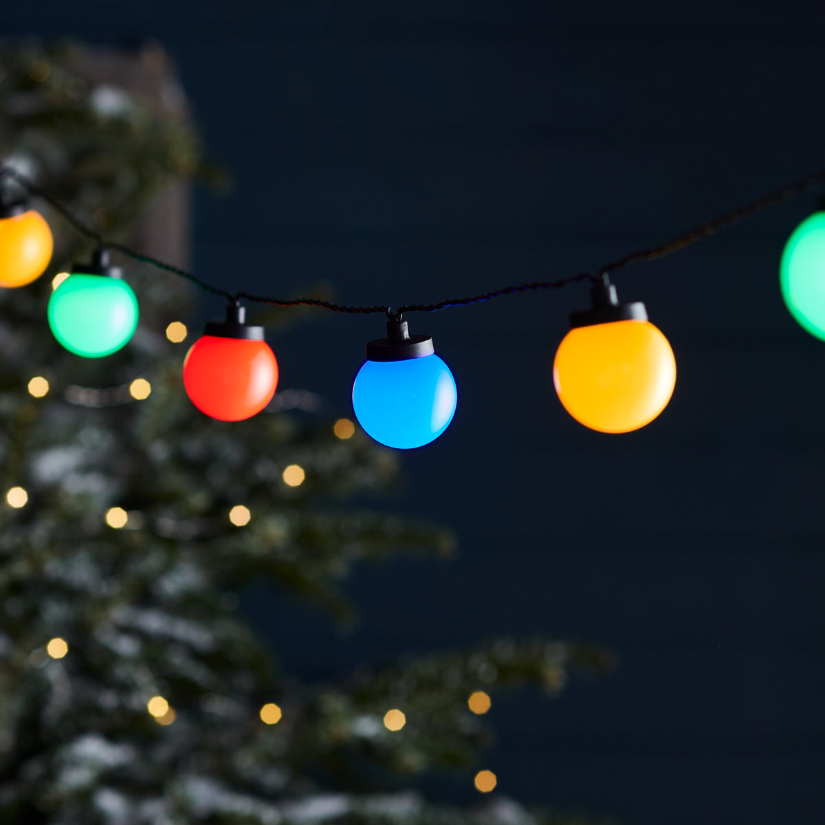 Bunte LED-Kugellichter in Gelb, Blau, Rot und Grün leuchten nachts an Lichterkette im Garten