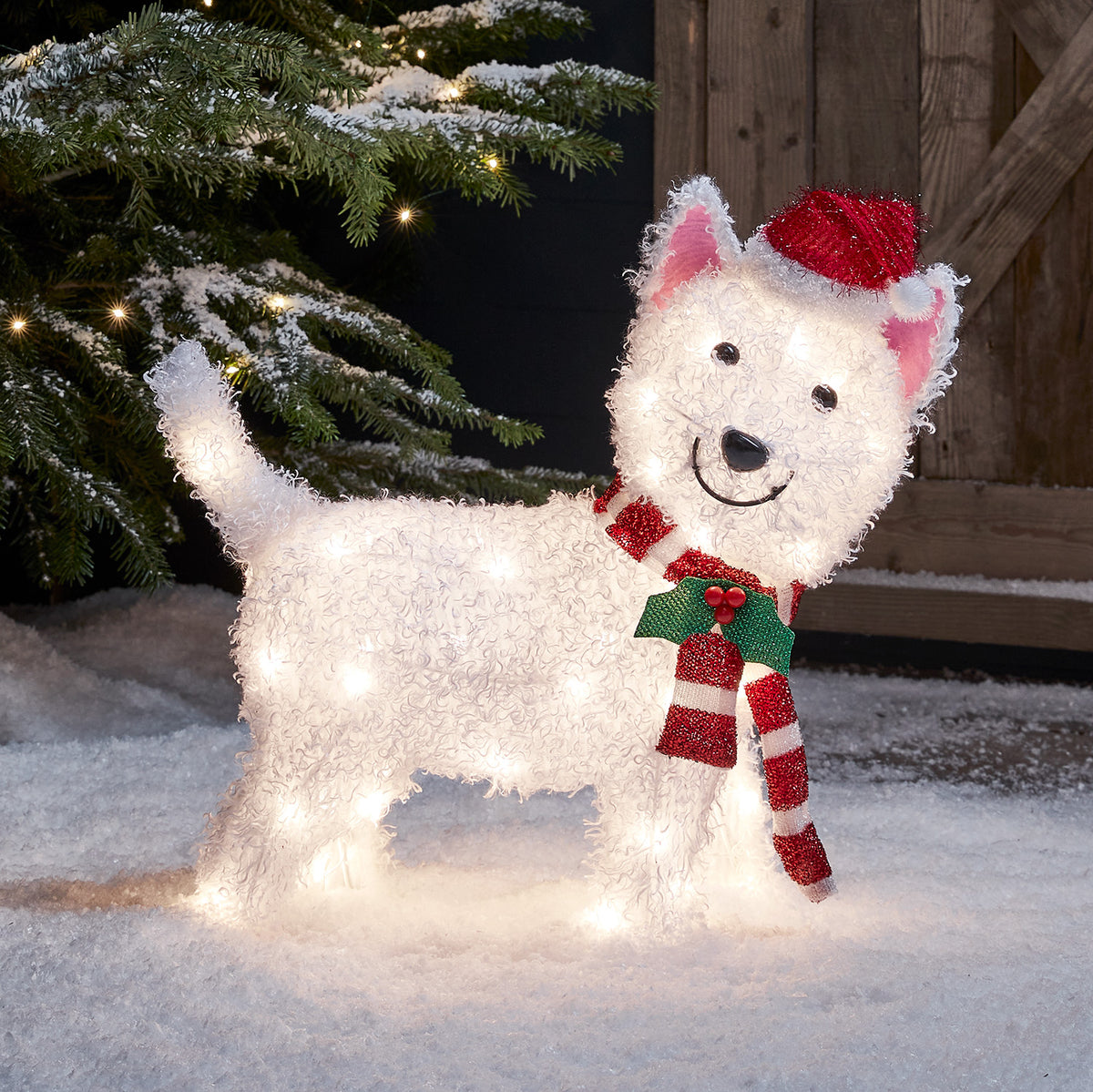 Weihnachtsfigur Westie mit roter Mütze und rot-weißem Schal beleuchtet im Schnee