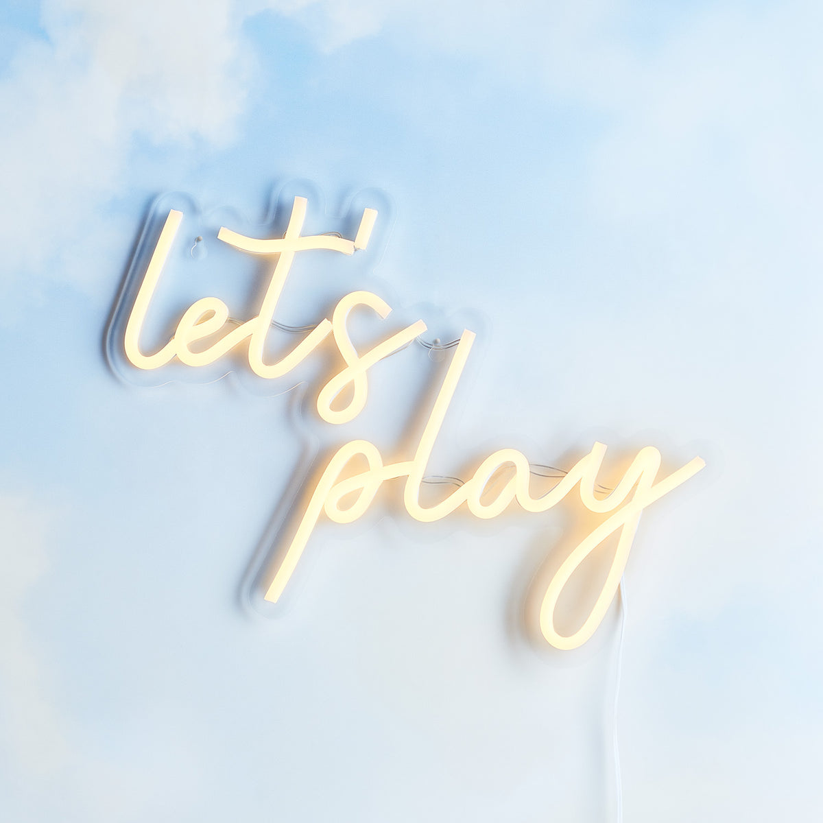 LED Neon Schriftzug 'Let's Play' leuchtet warmweiß an einer hellblauen Wand