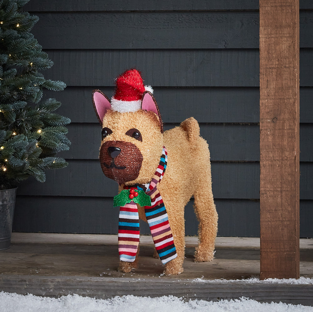 LED Weihnachtsfigur Bulldogge mit Weihnachtsmütze und buntem Schal auf Holzterrasse mit Schnee