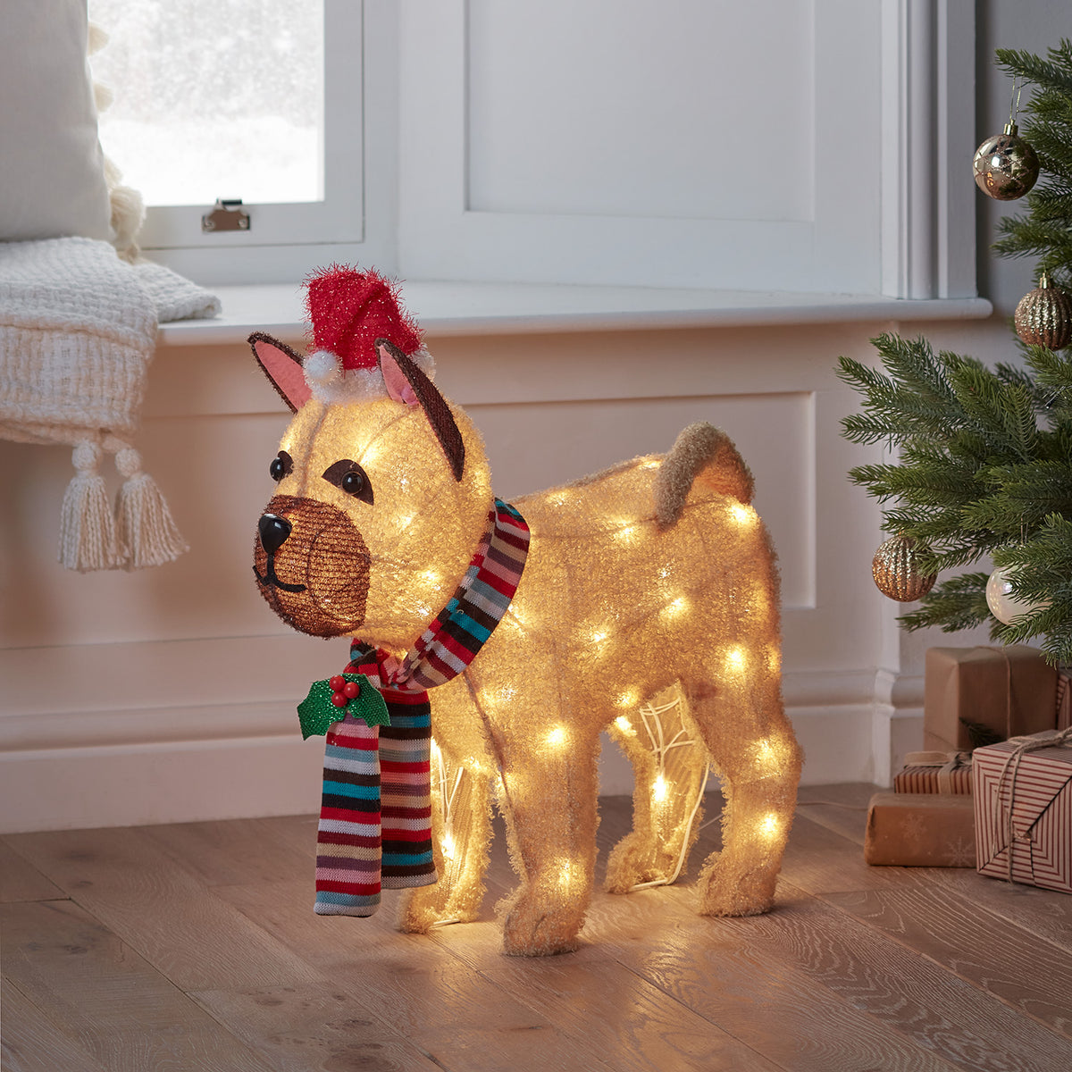 Beleuchtete Bulldoggen-Weihnachtsfigur mit Mütze und Schal neben Weihnachtsbaum und Geschenken